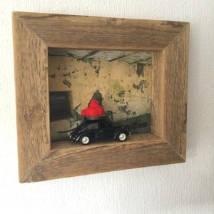 Könnte beinhalten: Ein schwarzes Spielzeugauto mit einem roten Herzen darauf, ausgestellt in einem Holzrahmen mit einem verwitterten Hintergrund.