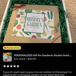 May include: A gift box with a seed packet labeled "Mommy's Garden" featuring illustrations of vegetables. The box is filled with green paper shreds and has the text "To plant a garden is to believe in tomorrow" on the lid.