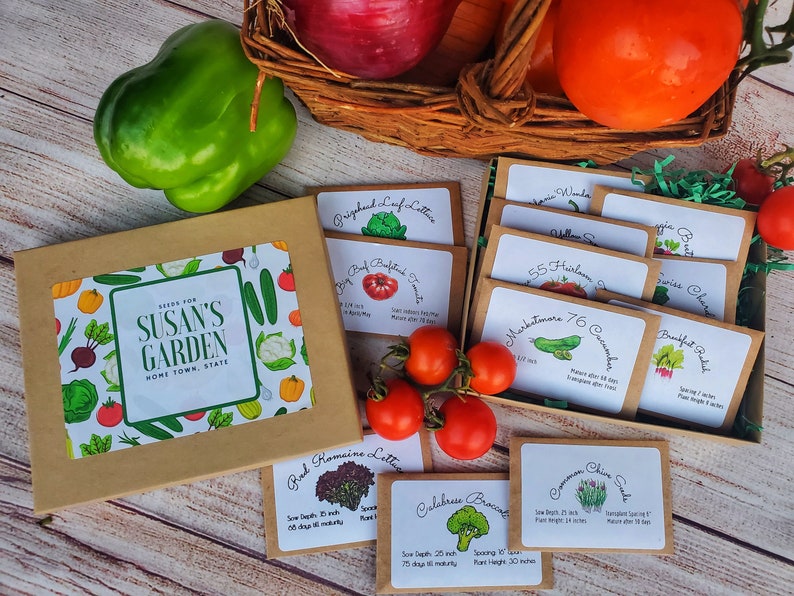 May include: A box set of garden seeds with a label that reads "Seeds for Susan's Garden". The set includes various seed packets for vegetables like tomatoes, lettuce, and cucumbers. Fresh produce, including tomatoes and a green bell pepper, are also in the image.