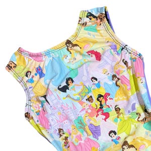May include: A sleeveless leotard featuring a colorful print of various Disney princesses. The design includes images of Jasmine, Snow White, Ariel, and other characters, set against a pastel background with castles and other fairytale elements.