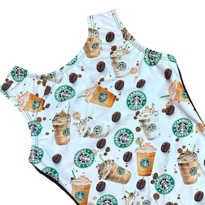 May include: White sleeveless leotard with a black trim. The leotard has a repeating pattern of coffee cups with whipped cream and the Starbucks logo. The background is white with brown coffee splatters.