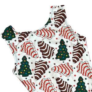 May include: White one-piece swimsuit with a festive Christmas tree pattern. The design features green Christmas trees with colorful ornaments, brown gingerbread-style trees with red stripes, and small star accents. The swimsuit has a scoop neckline and a sleeveless design.