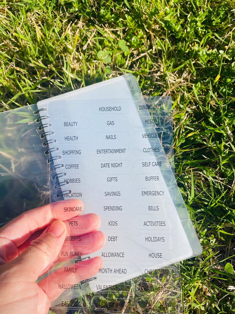 Peut inclure: Une feuille de plastique transparente avec des &eacute;tiquettes pour la budg&eacute;tisation et le suivi des d&eacute;penses. Les &eacute;tiquettes comprennent des cat&eacute;gories telles que les &eacute;piceries, le m&eacute;nage, les restaurants, la beaut&eacute;, la sant&eacute;, les achats, les loisirs, les v&ecirc;tements, le caf&eacute;, les sorties en amoureux, les soins personnels, les loisirs, les cadeaux, la marge de s&eacute;curit&eacute;, les vacances, les &eacute;conomies, les urgences, les soins de la peau, les d&eacute;penses, les factures, les animaux de compagnie, les enfants, les activit&eacute;s, les re&ccedil;us, les dettes, les vacances, l'argent de poche, l'allocation, la maison, la famille, le mois &agrave; venir, No&euml;l, Halloween, la Saint-Valentin et Thanksgiving.