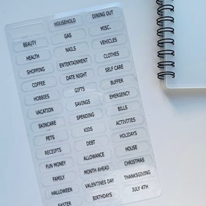 Peut inclure: Une feuille d'autocollants transparents avec des &eacute;tiquettes de texte blanches pour le budget et le suivi des d&eacute;penses. Les &eacute;tiquettes comprennent des cat&eacute;gories telles que m&eacute;nage, d&icirc;ner au restaurant, beaut&eacute;, sant&eacute;, shopping, caf&eacute;, loisirs, vacances, soins de la peau, animaux de compagnie, re&ccedil;us, argent de poche, famille, Halloween, P&acirc;ques, essence, ongles, divertissement, rendez-vous galant, cadeaux, &eacute;conomies, d&eacute;penses, enfants, dettes, allocation, mois &agrave; venir, Saint-Valentin, anniversaires, divers, v&eacute;hicules, v&ecirc;tements, soins personnels, tampon, urgence, factures, activit&eacute;s, vacances, maison, No&euml;l, Thanksgiving et 4 juillet.