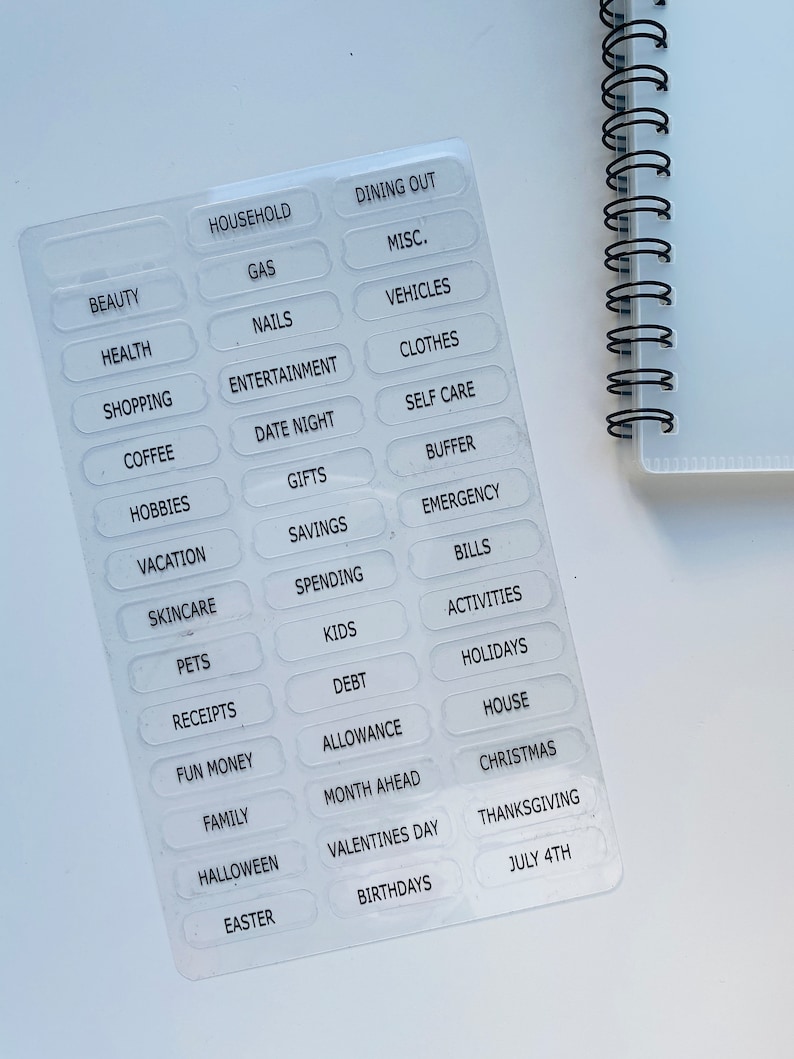 Peut inclure: Une feuille d'autocollants transparents avec des &eacute;tiquettes de texte blanches pour le budget et le suivi des d&eacute;penses. Les &eacute;tiquettes comprennent des cat&eacute;gories telles que m&eacute;nage, d&icirc;ner au restaurant, beaut&eacute;, sant&eacute;, shopping, caf&eacute;, loisirs, vacances, soins de la peau, animaux de compagnie, re&ccedil;us, argent de poche, famille, Halloween, P&acirc;ques, essence, ongles, divertissement, rendez-vous galant, cadeaux, &eacute;conomies, d&eacute;penses, enfants, dettes, allocation, mois &agrave; venir, Saint-Valentin, anniversaires, divers, v&eacute;hicules, v&ecirc;tements, soins personnels, tampon, urgence, factures, activit&eacute;s, vacances, maison, No&euml;l, Thanksgiving et 4 juillet.