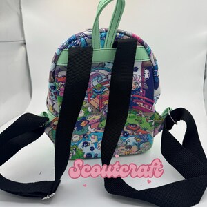 May include: Miniature backpack with a colorful anime-style print featuring various characters and scenes. The backpack has black straps and a mint green handle and trim. The text "Scoutcraft" is printed in pink script across the bottom.
