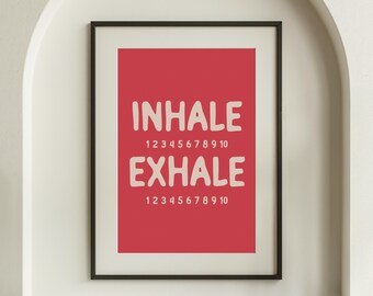 May include: Framed art print with a red background and the words "INHALE" and "EXHALE" in large, off-white letters. Below each word are the numbers 1 through 10. The black frame adds a modern touch to this mindfulness-themed wall art.