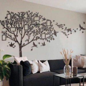 May include: A contemporary living room featuring a black corner sofa, a circular black footstool with a cream throw, and a glass-topped coffee table. A wall decoration of a tree with picture frames and birds.