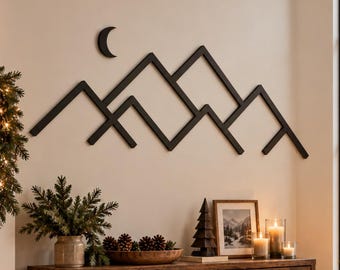 May include: A black metal wall art piece featuring a geometric mountain range silhouette and a crescent moon shape. The linear design is mounted on a plain wall, showcasing sharp, angular peaks and a minimalist aesthetic that spans across the wall space.