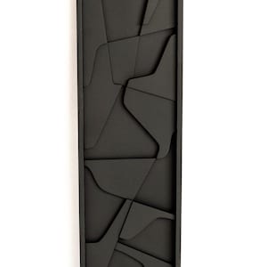 May include: Black wooden wall art with a geometric design. The art is made of multiple pieces of wood that are cut into different shapes and sizes. The wood is painted black and the pieces are arranged in a random pattern.