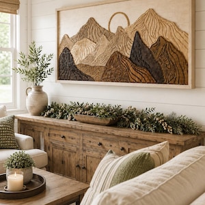 May include: A rectangular wooden wall art piece featuring a carved mountain landscape with a circular sun element. The artwork displays layered textures in shades of light beige, medium brown, and dark charcoal, framed in a light wood border.