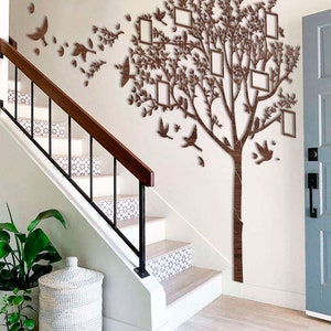 May include: A wooden wall decoration featuring a tree design with integrated photo frames and bird silhouettes. The brown tree has multiple rectangular frames for photos. Decorative birds are positioned around the tree, creating a wall art display.