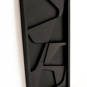 May include: Black wall art with a geometric design. The art is made of wood and has a 3D effect.