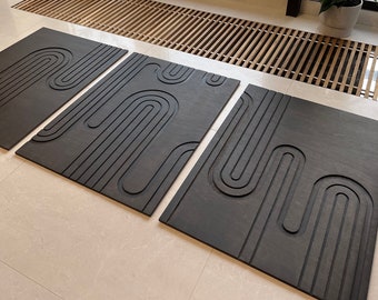 May include: Three black rectangular wall panels with a raised geometric pattern of curved lines. The panels are arranged in a row on a light beige floor.