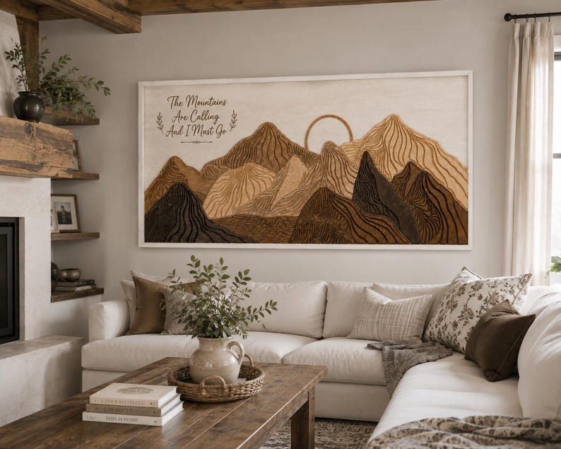Puede incluir: Una pieza de arte mural rectangular de madera con un paisaje monta&ntilde;oso en capas en tonos marr&oacute;n y bronceado. La obra incluye el contorno de un sol y el texto The Mountains Are Calling And I Must Go en una fuente cursiva oscura a la izquierda.