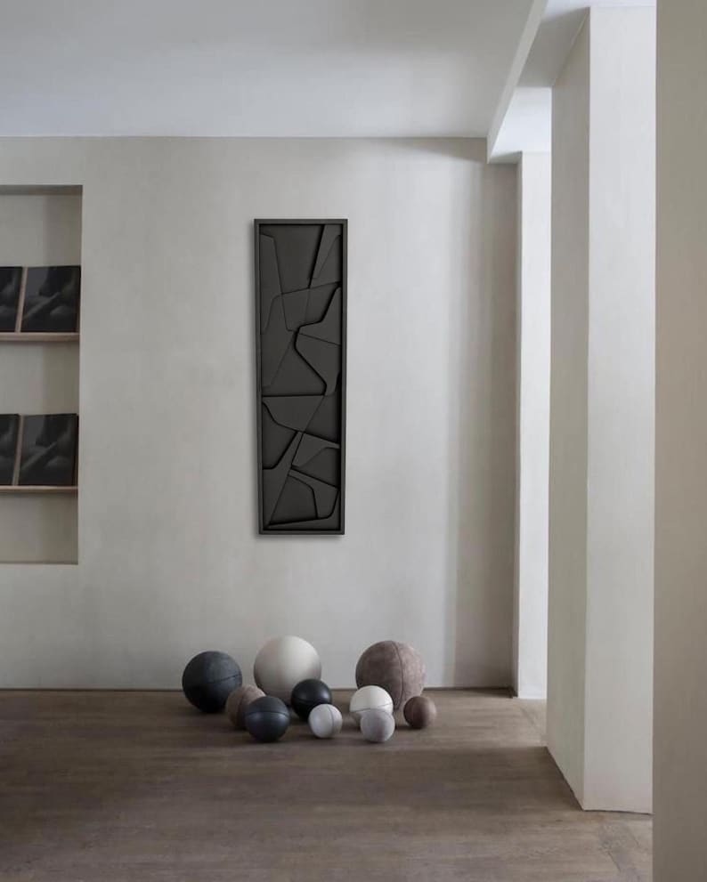 May include: A minimalist living room with a black framed abstract wall art piece and a collection of round, textured, gray and white balls on the floor.