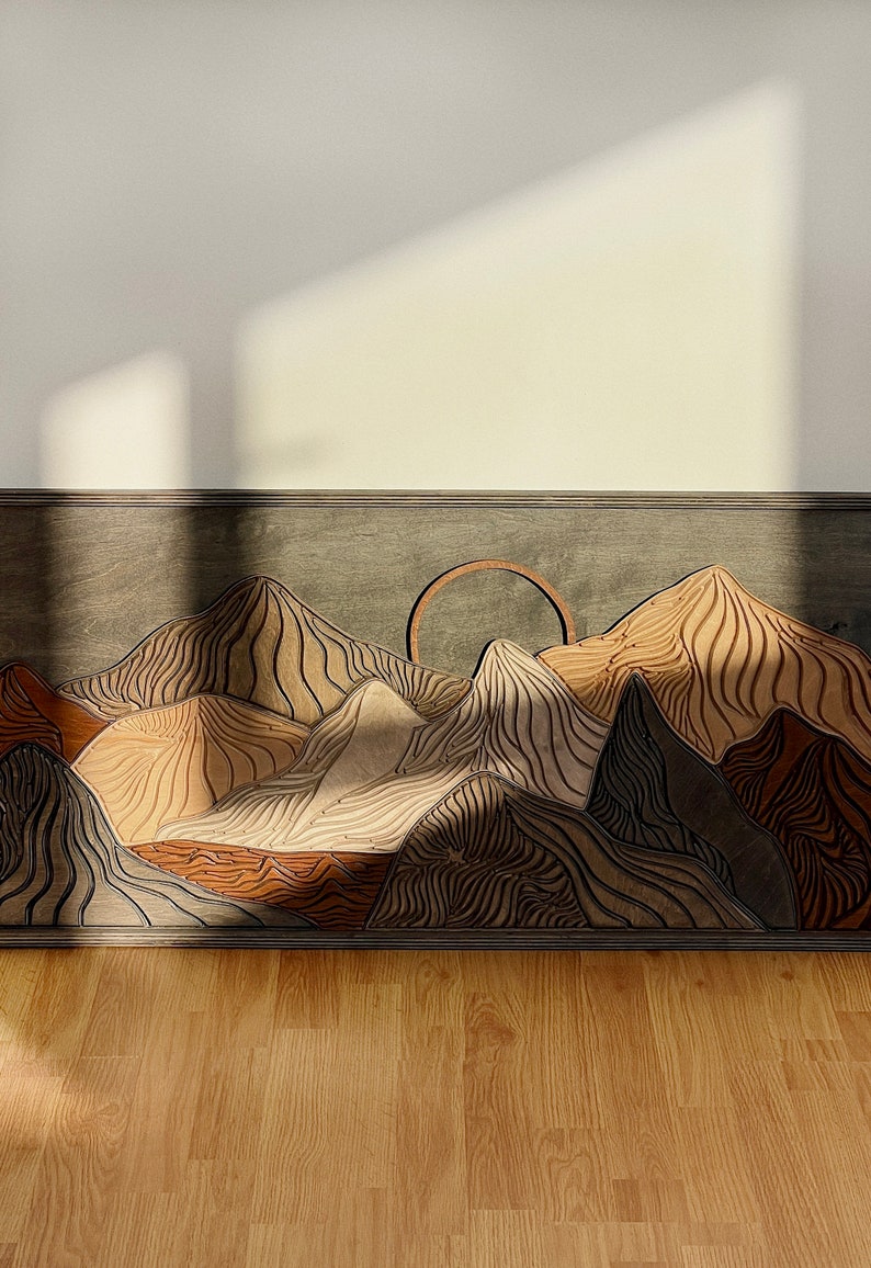 Puede incluir: Una pieza de arte mural rectangular de madera que presenta un paisaje monta&ntilde;oso en capas con un elemento solar circular. El dise&ntilde;o incorpora varios tonos de madera, incluyendo bronceado claro, marr&oacute;n oscuro y gris, con intrincados patrones de l&iacute;neas topogr&aacute;ficas talladas.