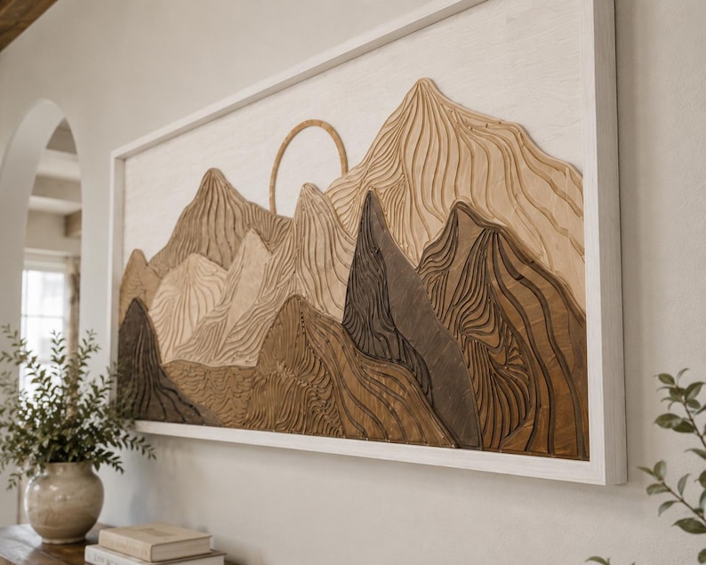 Puede incluir: Una pieza de arte mural rectangular que presenta un paisaje monta&ntilde;oso de madera en capas con un elemento solar circular. La obra muestra varios tonos de madera marr&oacute;n y bronceada con texturas onduladas talladas, todo dentro de un marco de madera blanco.
