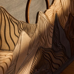 Puede incluir: Un panel decorativo de madera para pared que presenta un paisaje de monta&ntilde;a tallado con picos en capas y surcos profundos y texturizados. El dise&ntilde;o incluye un prominente elemento de arco circular de madera sobre la silueta central.