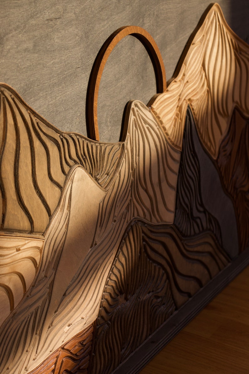 Puede incluir: Un panel decorativo de madera para pared que presenta un paisaje de monta&ntilde;a tallado con picos en capas y surcos profundos y texturizados. El dise&ntilde;o incluye un prominente elemento de arco circular de madera sobre la silueta central.