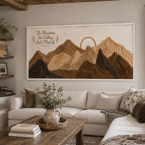 May include: A rectangular wooden wall art piece featuring a layered mountain landscape in shades of brown and tan. The artwork includes a circular sun outline and the text The Mountains Are Calling And I Must Go in a dark script font on the left side.
