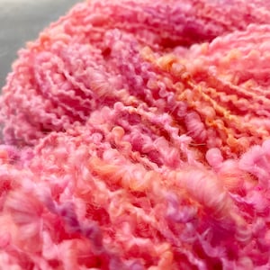 May include: A close-up of a pink and orange yarn with a fluffy texture. The yarn is made of soft fibres and is perfect for knitting or crocheting.