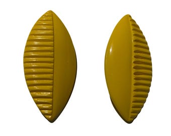 May include: A pair of yellow leaf-shaped hair clips. The clips have a ribbed texture on one side and a smooth surface on the other.