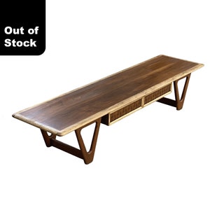 May include: A mid-century modern coffee table with a walnut wood top and two woven drawers. The table has a unique, angled, A-frame base.