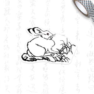 May include: A black and white sticker featuring a rabbit illustration in a minimalist style. The rabbit is depicted in a sitting position with its ears perked up. A roll of black and white polka dot washi tape and a green pencil are in the background.