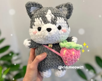 May include: A gray and white crocheted husky plush toy with a pink and green crocheted strawberry attached to a strap. The toy is being held by a hand with a small tattoo on the wrist. The text "@rin.meow21" is visible in the bottom right corner of the image.