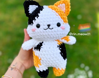 May include: A crocheted calico cat toy with black, white, and orange yarn. The cat has a cute, cartoon-like face with black eyes and a pink nose.