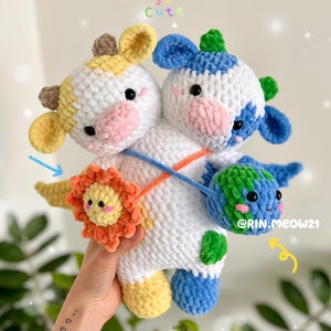 Pode incluir: Um brinquedo de pelúcia de vaca de crochê com um rosto amarelo e azul, segurando um sol e uma terra de crochê. O brinquedo é branco com manchas amarelas e azuis. O texto "So Cute" está escrito acima do brinquedo. O texto "@RIN.MEOW21" está escrito abaixo do brinquedo.