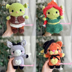 May include: Four handmade crochet dolls: a green ogre with a brown vest, a green doll with red hair, a gray donkey with a white heart, and an orange cat with a black hat. Each doll has black eyes and is holding a pose.