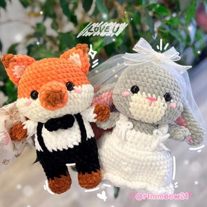May include: A crocheted orange fox wearing a black bow tie and suspenders stands next to a crocheted gray bunny wearing a white dress and veil. The fox and bunny are holding hands and the text "LOVE U" is written above them. The text "@rin.meow21" is written below them.
