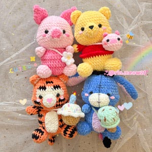 May include: Four crocheted stuffed animals: a pink pig, a yellow bear holding a smaller pink pig, an orange and white tiger holding a cupcake, and a blue bunny holding an ice cream cone.  The animals are all smiling and have cute faces.