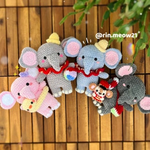 May include: Five crocheted elephant plushies in different colours and poses. The elephants are wearing hats and scarves. One elephant is holding a ball. The elephants are on a wooden background. @rin.meow21