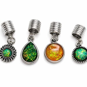 May include: Four silver-toned hair beads with dangling charms. Two charms are round with green iridescent inlays, one is a teardrop shape with green glitter, and one is a round orange iridescent charm. Each bead features a coiled metal design.