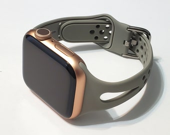 May include: A gold Apple Watch with a grey silicone sport band. The band has a perforated design and a buckle closure.