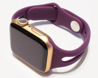 May include: A gold Apple Watch with a purple silicone sport band. The band has a single loop design and a magnetic closure.