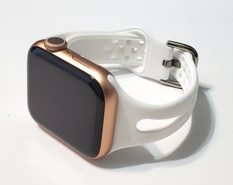 May include: A gold Apple Watch with a white silicone sport band. The band has a perforated design and a silver buckle.