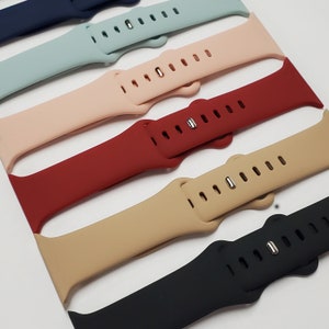 May include: Five different colored silicone watch bands. The bands are arranged in a stack, with the darkest band at the bottom and the lightest band at the top. The bands are all the same size and have a similar design.