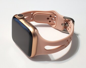 May include: A rose gold Apple Watch with a light pink silicone sport band. The band has a perforated design and a buckle closure.