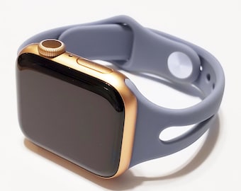 May include: A gold Apple Watch with a grey silicone sport band. The band has two cutouts on the side.