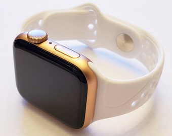 May include: A gold Apple Watch with a white silicone band. The band has a textured design with holes for ventilation.