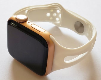 May include: A gold Apple Watch with a white sport band. The band has a perforated design for breathability.