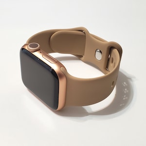 May include: A gold Apple Watch with a tan silicone band. The watch face is black and the band is made of a soft, flexible material.