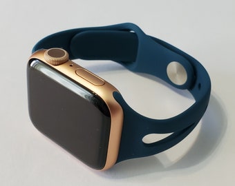 May include: A gold Apple Watch with a dark blue silicone sport band. The band has a unique design with a cutout on the bottom.