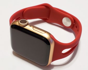May include: A gold Apple Watch with a red silicone sport band. The watch face is black and the band has a cut-out design.