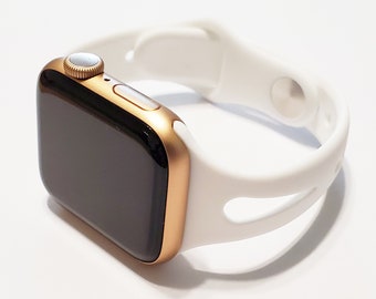 May include: A gold Apple Watch with a white sport band. The watch face is black and the band has a unique design with cutouts.