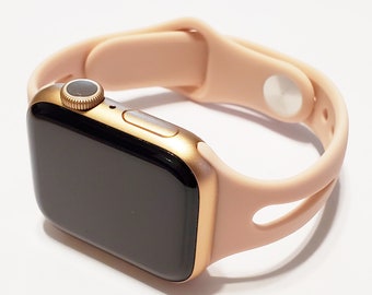 May include: A gold Apple Watch with a pink silicone strap. The strap has a cut-out design and a silver buckle.